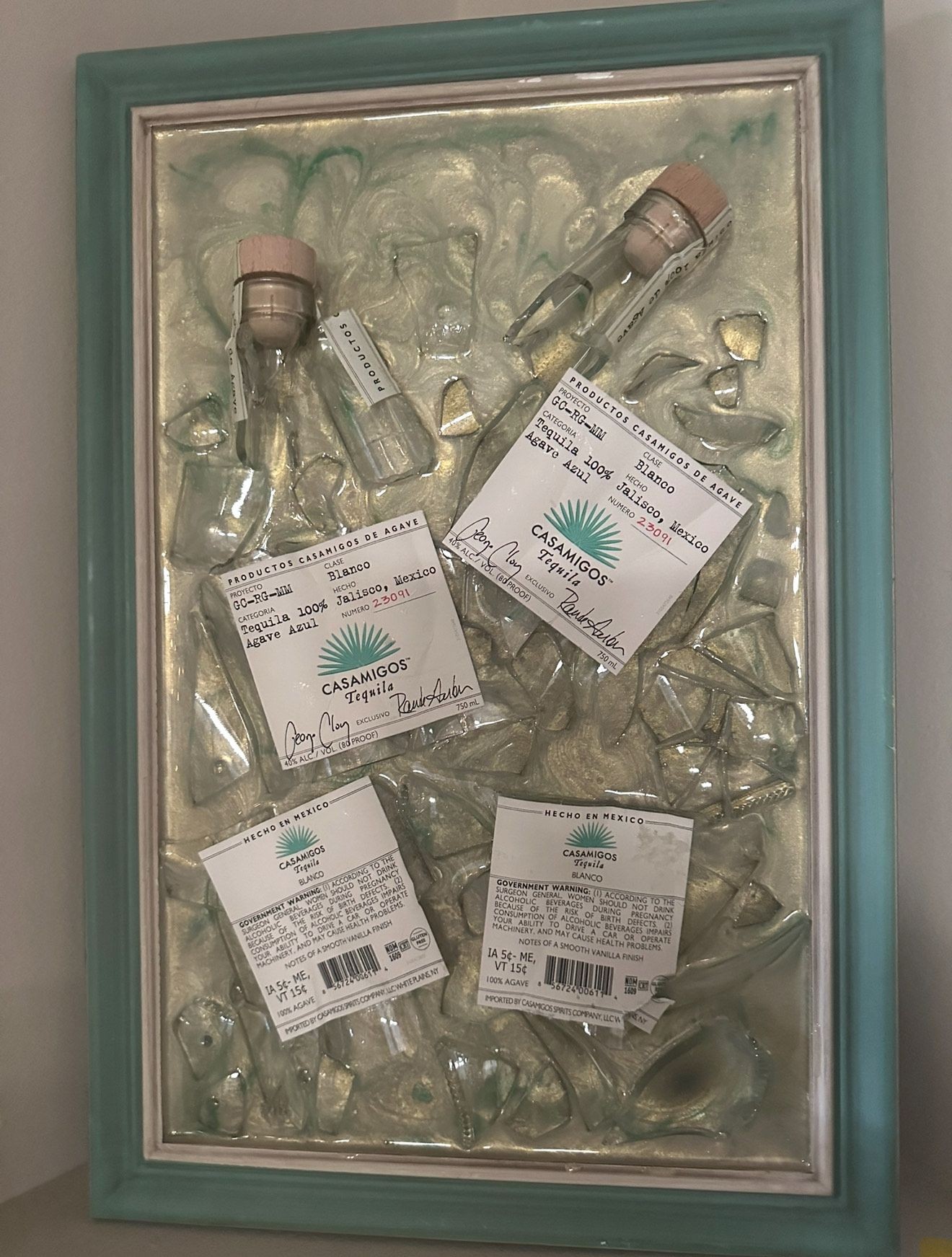 Framed display of broken glass bottles and Casamigos tequila labels.
